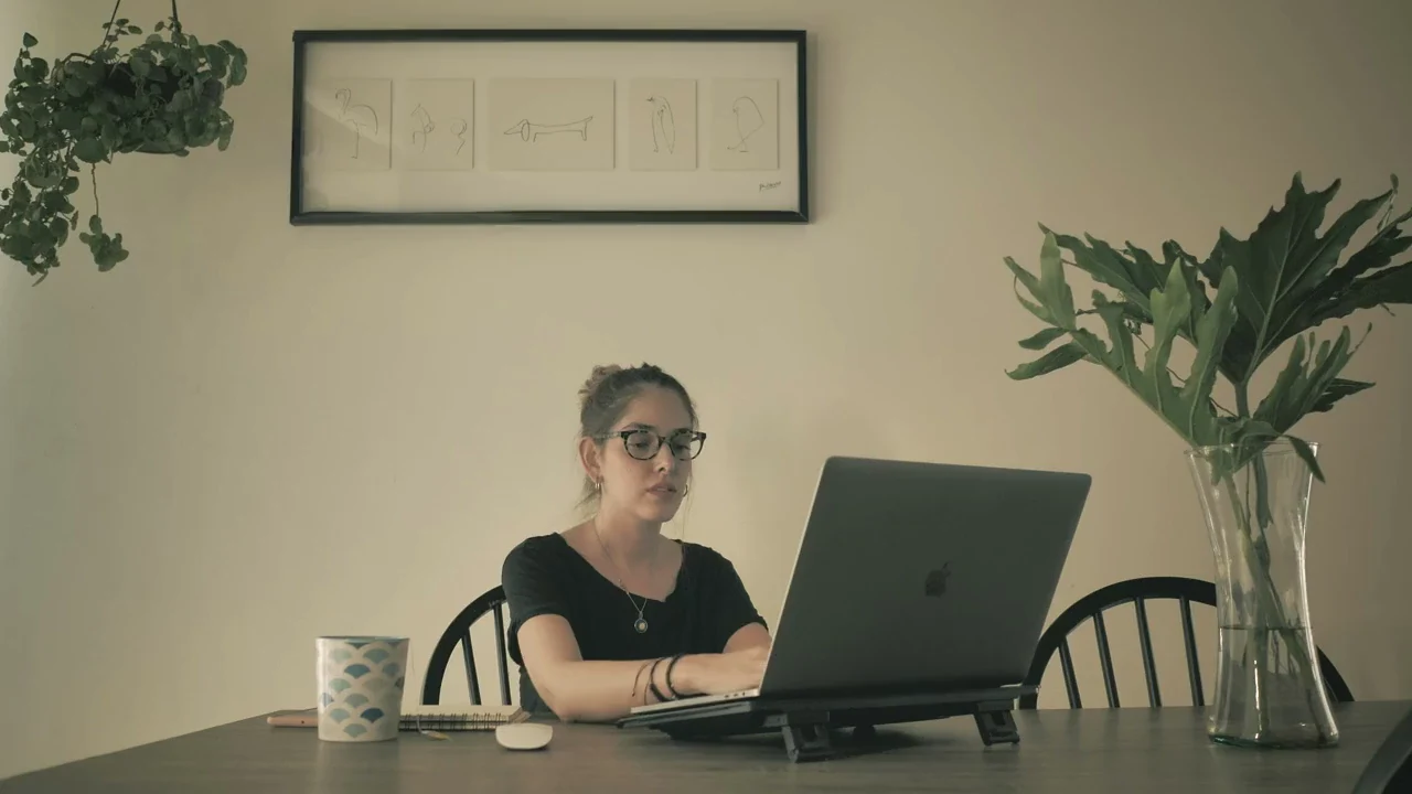 Žena radi na laptopu za drvenim stolom u toplom, mirnom radnom prostoru.